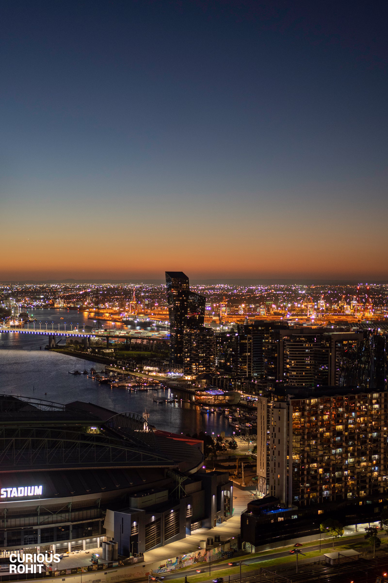 A cityscape at dusk with a large building and boats in the water.