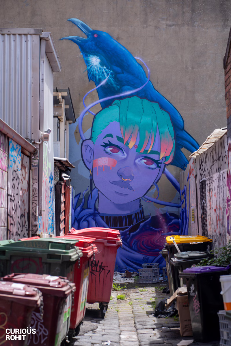 A girl with a nose ring and a blue shirt with a red trash can in the background