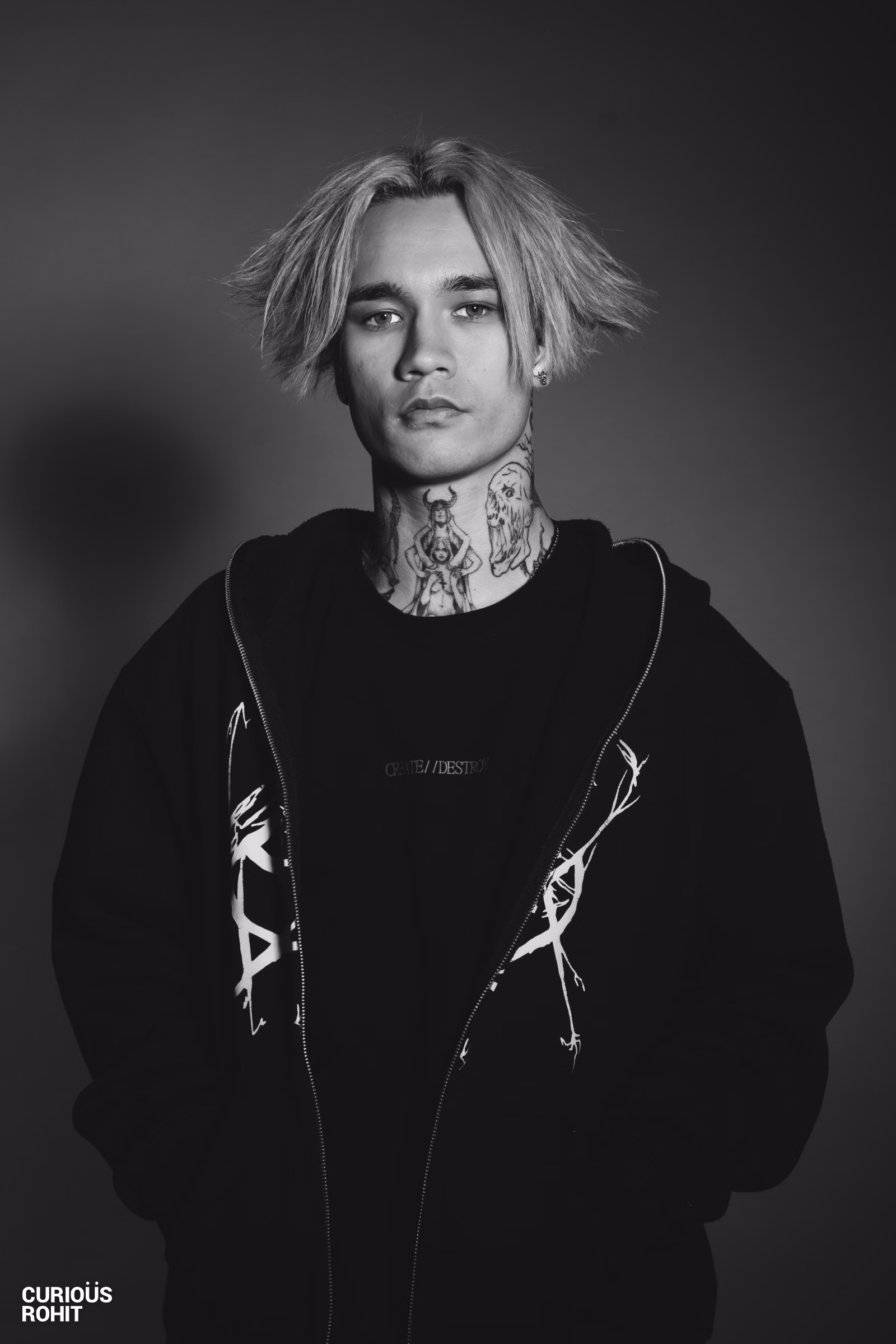 A man with a tattooed neck and spiky hair wearing a black jacket